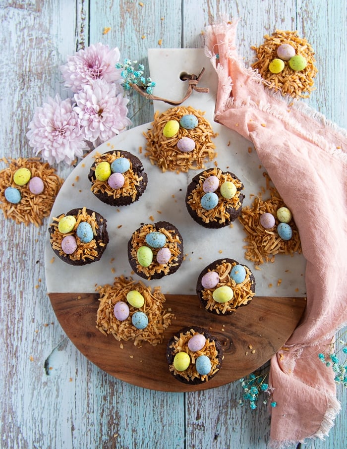 coconut brownies on a wooden board all topped and ready with coconut shreds and chocolate eggs