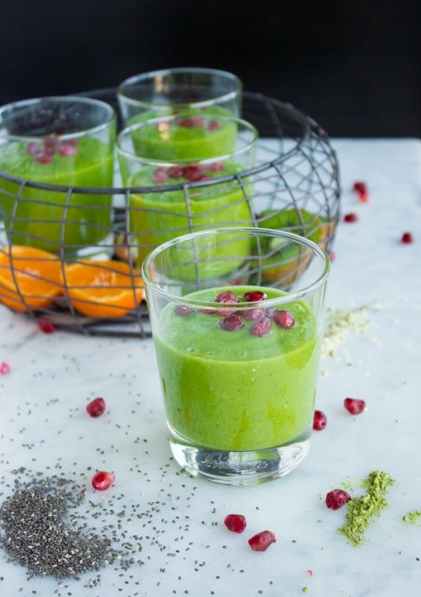 side view of 4 glasses of green hemp matcha kale power boosting smoothie on a white tabletop.