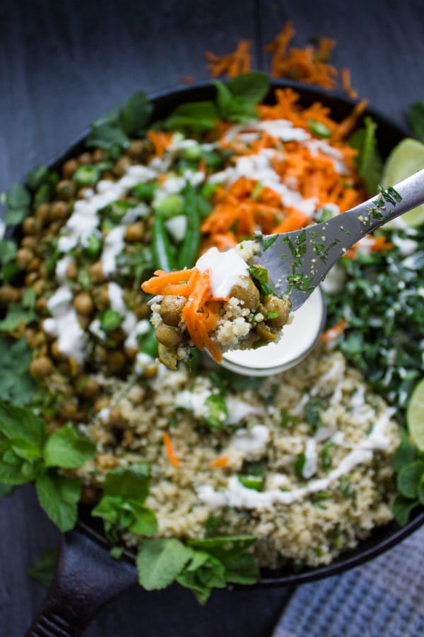A fork holding spicy chickpeas, Moroccan couscous, carrot salad and tahini sauce over the plate of couscous salad.