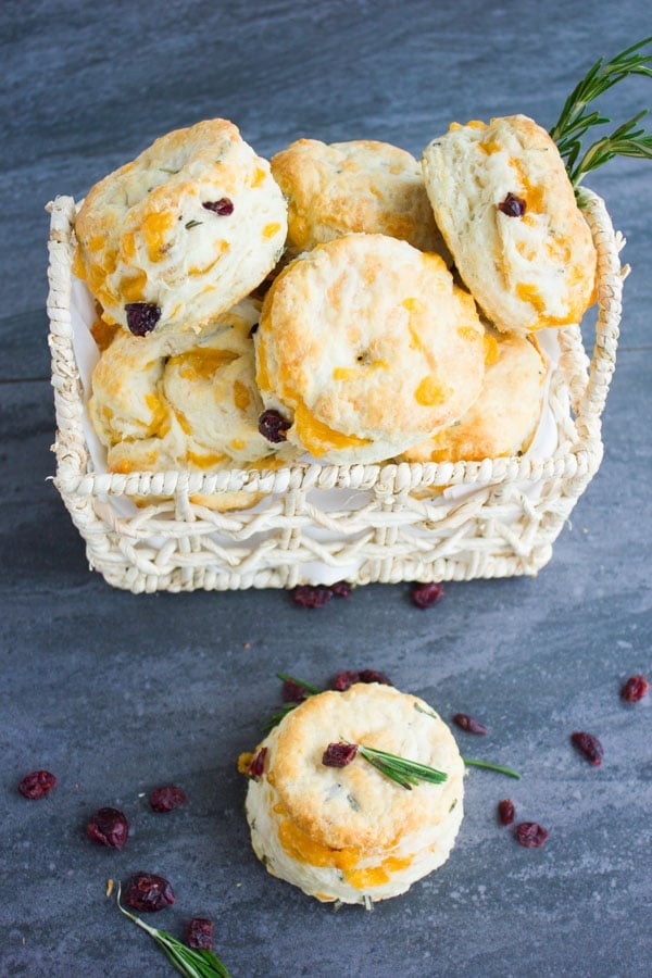 Homemade Buttermilk Biscuits With Cheddar Rosemary & Cranberries in a basket with some biscuits lying in front of it