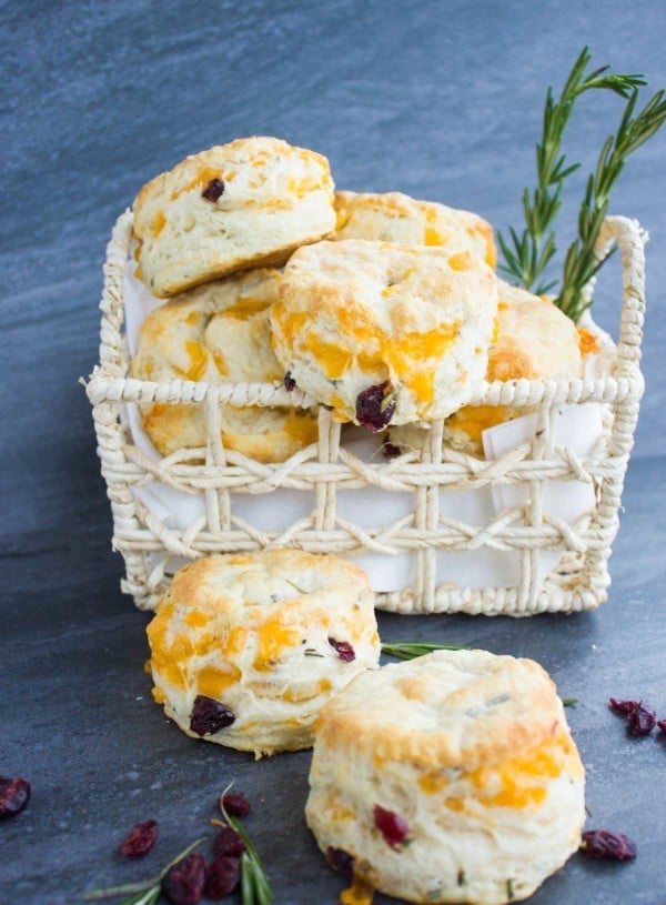 Homemade Buttermilk Biscuits With Cheddar Rosemary & Cranberries in a basket with some biscuits lying in front of it