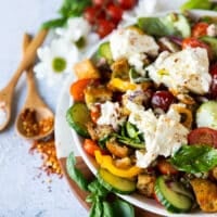 side view of a half plate of panzanella salad showing the ingredients of the salad and some fresh tomatoes, basil and chilli flakes on the board