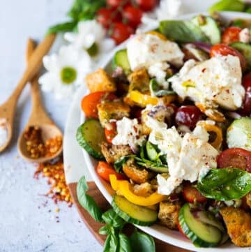 side view of a half plate of panzanella salad showing the ingredients of the salad and some fresh tomatoes, basil and chilli flakes on the board