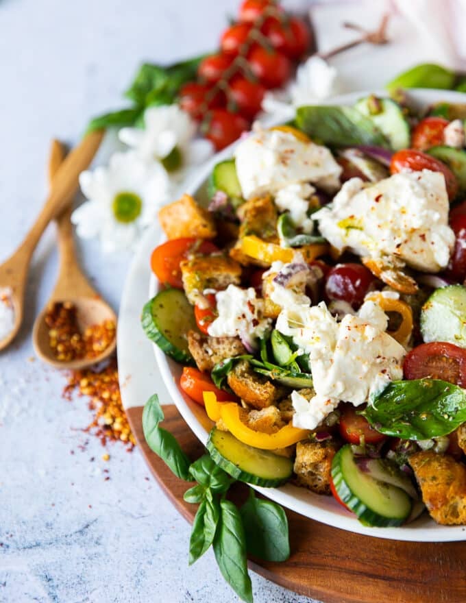 side view of a half plate of panzanella salad showing the ingredients of the salad and some fresh tomatoes, basil and chilli flakes on the board