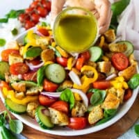 A hand pouring the panzanella salad dressing over the panzanella salad