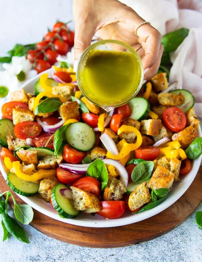 A hand pouring the panzanella salad dressing over the panzanella salad 