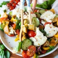 A hand scooping panzanella salad using two salad spoons