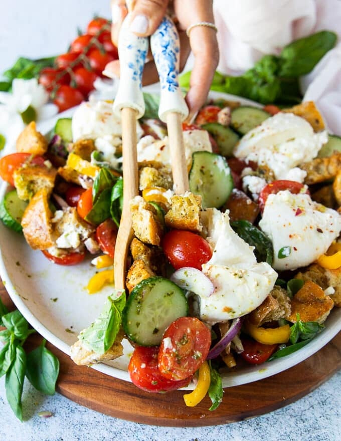 A hand scooping panzanella salad using two salad spoons