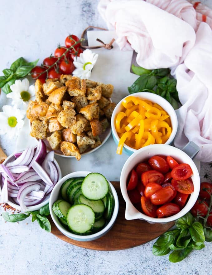 ingredients for panzanella salad including the bread, tomatoes, sweet bell peppers, onions, cucumbers and plenty of basil leaves