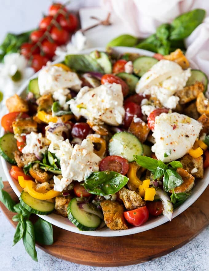 close up of the finished panzanella salad with dressing and some burrata cheese on top