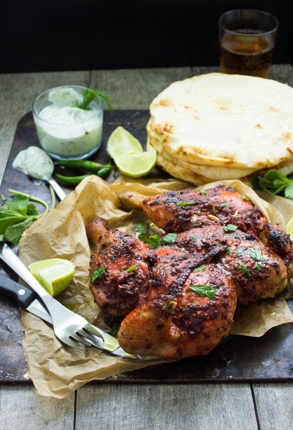 Quick a butterflied Roast Tandoori Chicken served on a black platter with naan bread and raita