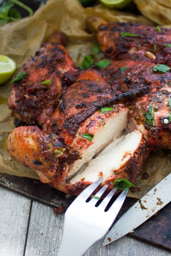 Quick Roast Tandoori Chicken on a black platter with a chunk being cut out off the breast to reveal juicy tender meat