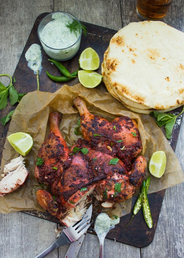 overhead of Quick Roast Tandoori Chicken on a black platter with yogurt dip and naan bread on the side