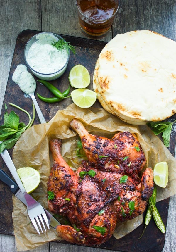 overhead shot of Quick Roast Tandoori Chicken served on a black platter surrounded with yogurt dip and naan bread