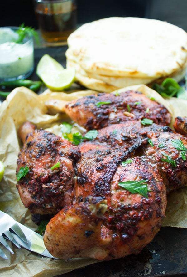 close-up of Quick Roast Tandoori Chicken served on parchment paper with a stack on naan bread in the background