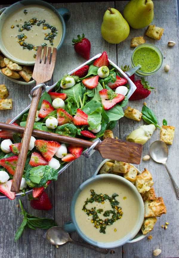 Strawberry Spinach Salad served in a boat-shaped silver bowl next to a bowl with Artichoke Soup and croutons.