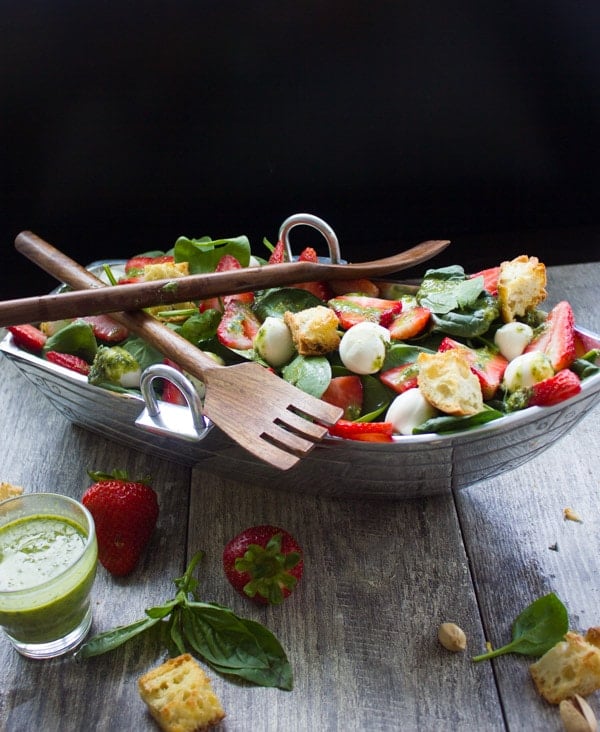 a boat-shaped dish with strawberry spinach salad on a wood table