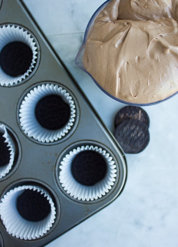 chocolate cheesecake filling in a bowl next to a muffin tin lined with oreos