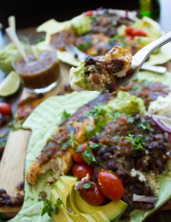 a fork balancing a bite of fried tilapia fish fillet with rice black beans and guacamole