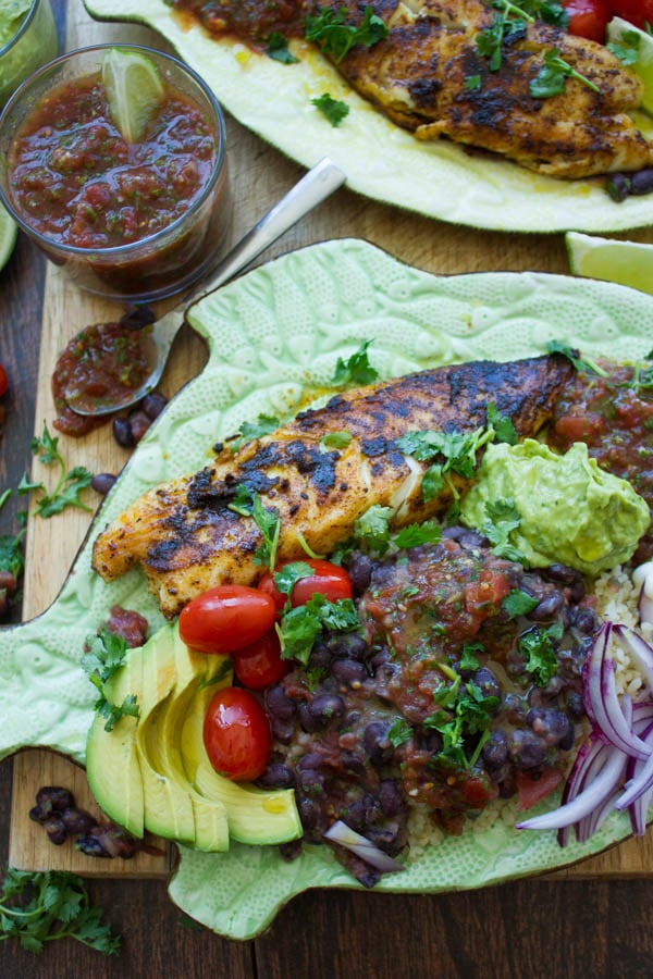 overhead of pan-fried tilapia fish fillets crusted with Mexican spices and served with black beans, guacamole and salsa on a fish shaped plate