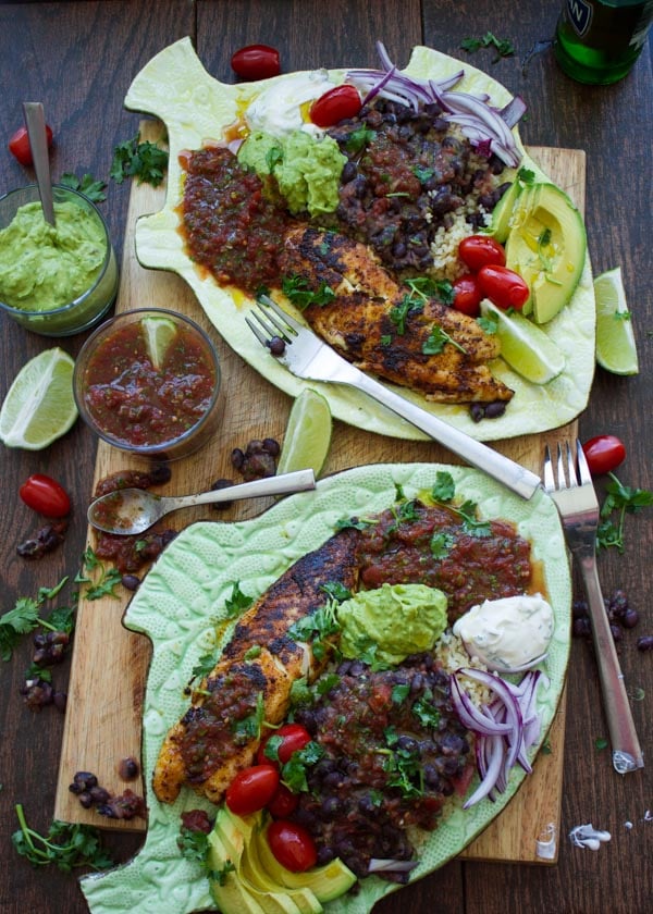 overhead shot of two plated loaded with pan-fried tilapia fillet, Mexican Black beans, restaurant-style salsa and guacamole