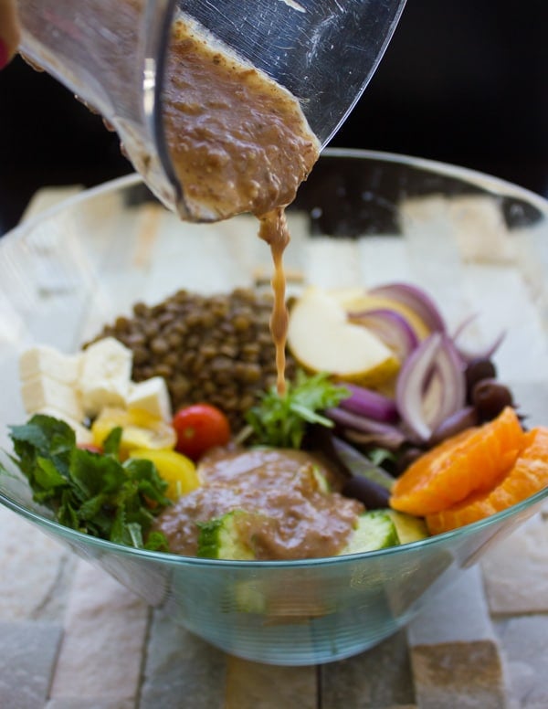 dressing being poured on top of Orange Lentil Greek Salad. 