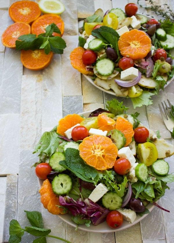 two bowls of Orange Lentil Greek Salad with chunks of feta, cocktail tomatoes and fresh mint leaves