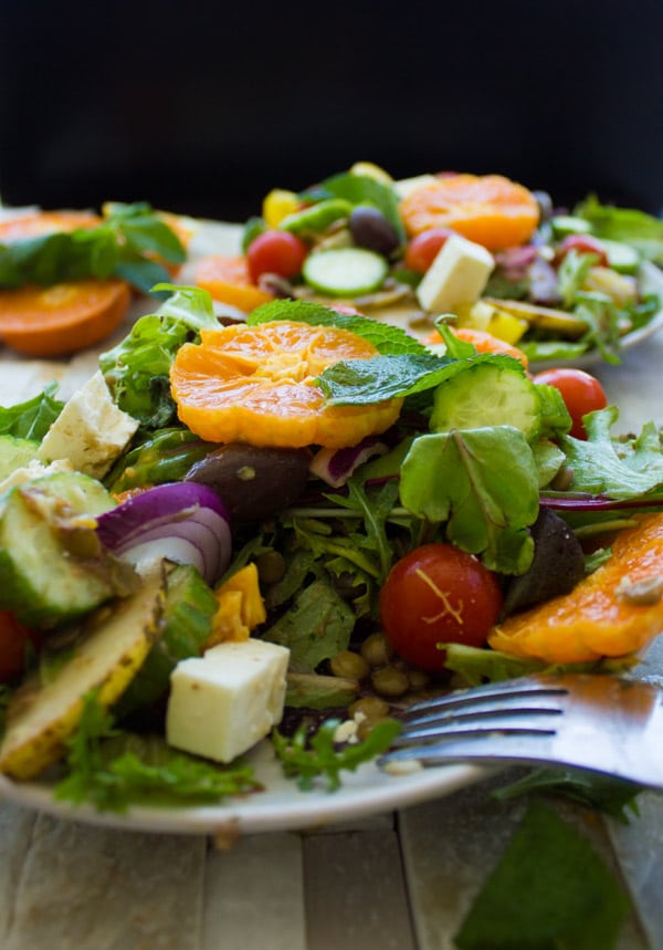 side view of a plate of Orange Lentil Greek Salad loaded with fresh fruit and vegetables