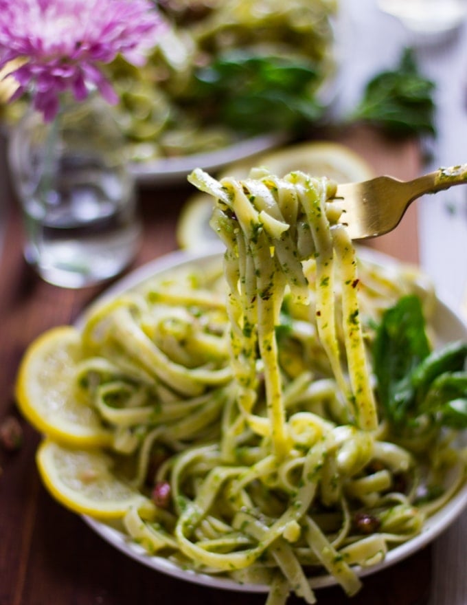 a fork stretching out some pesto pasta to show the specs of pistachio pesto over the pasta 