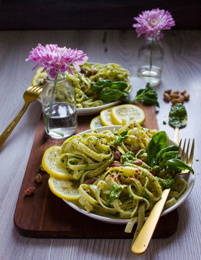 side view of a pesto pasta plate with a frok, some fresh basil and crunchy pistachios on top 