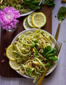 a bowl of pesto pasta with lemon slices and some fresh basil