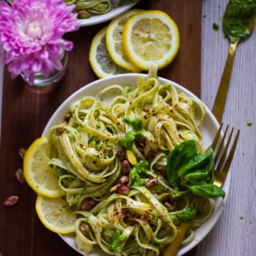 a bowl of pesto pasta with lemon slices and some fresh basil