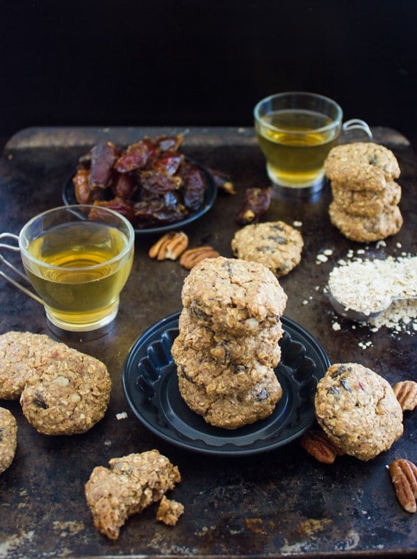 Vegan Oatmeal Raisin Cookies arranged on a rustic table with mugs of tea, pecans and dates