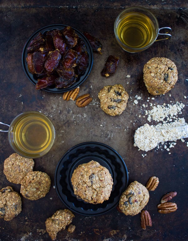 overhead shot of gluten-free Vegan Oatmeal Raisin Cookies on a table with tea mugs, dates and oats