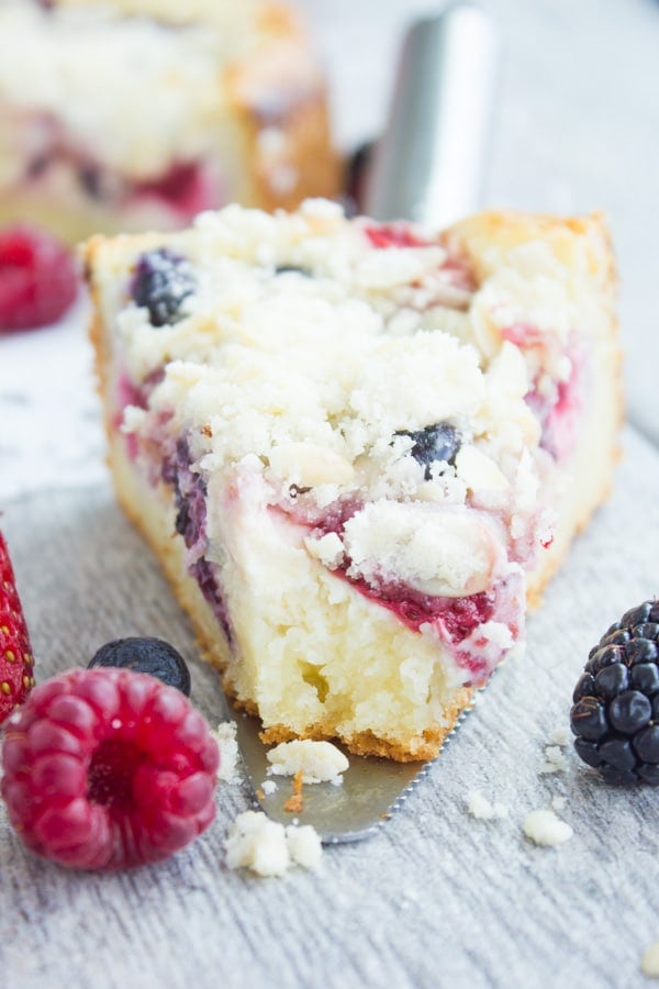 a slice of Cheesecake Streusel Raspberry Cake on a cake lifter with one bite missing 