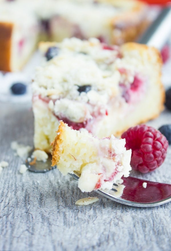 close-up of a fork-full of Cheesecake Streusel Raspberry Cake and a slice of cake in the background