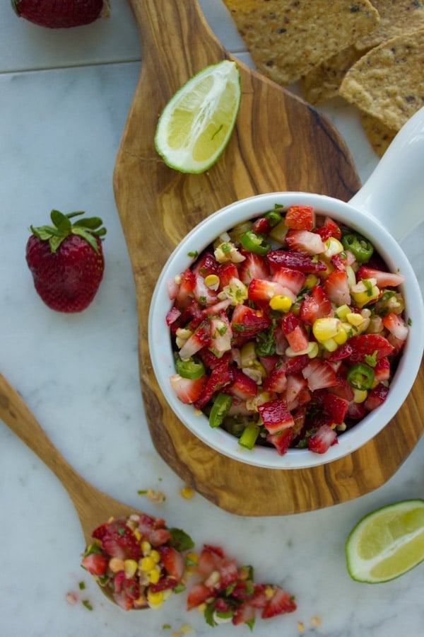 Strawberry Corn Salsa served in a small white bowl on a wooden board with some chips