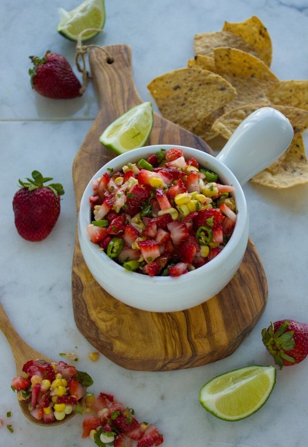 Fresh Strawberry Corn Salsa in a white bowl with a side of tortilla chips and some lime wedges