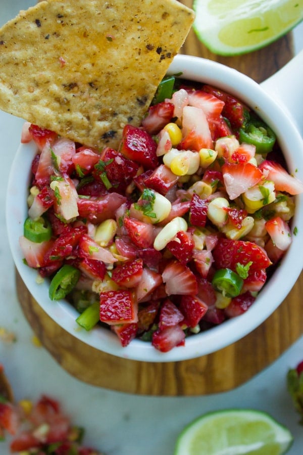 Strawberry Corn Salsa served in a white bowl with a tortilla chip dipped into it