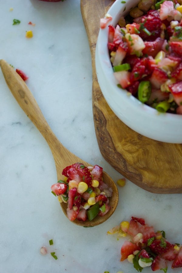 a wooden spoon loaded with strawberry corn salsa placed next to the salsa bowl