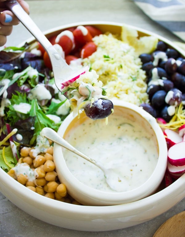 a fork full of cauliflower rice salad balanced over a big bowl filled with cauliflower rice salad.