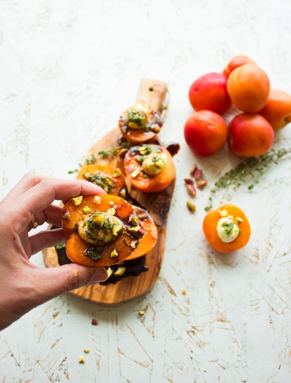 a hand holding a pistachio-sprinkled mozzarella stuffed apricot half into the camera