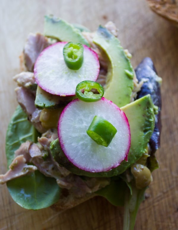 an open tuna sandwich topped with radishes, avocado slices and green onions