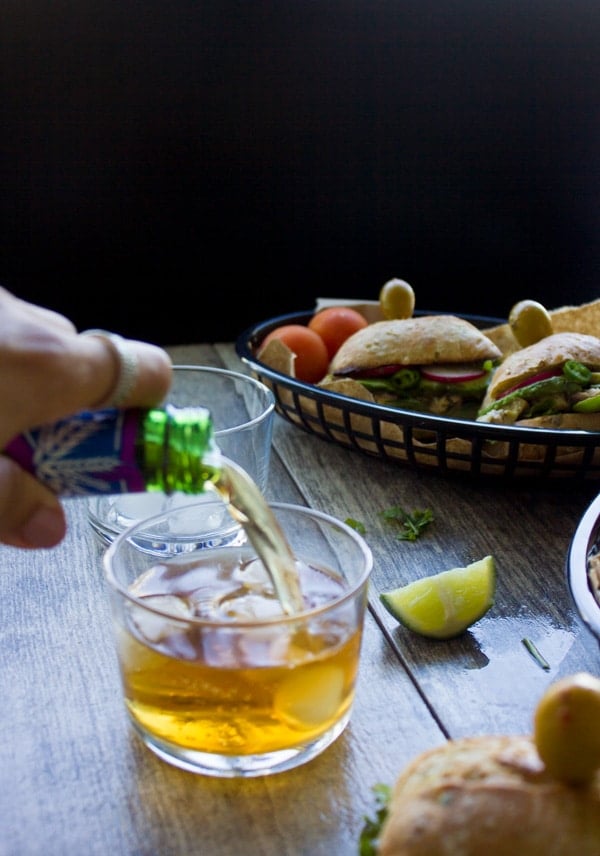 a drink being poured into a glass with a basket of tuna sandwiches in the background