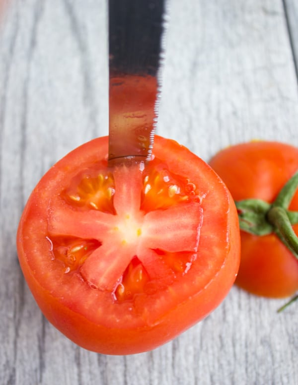 a knife cutting around the inside of a tomato to hollow it out