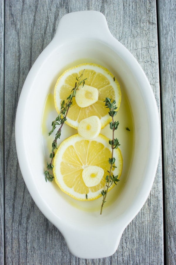 thyme, lemon and garlic slices in a white casserole dish