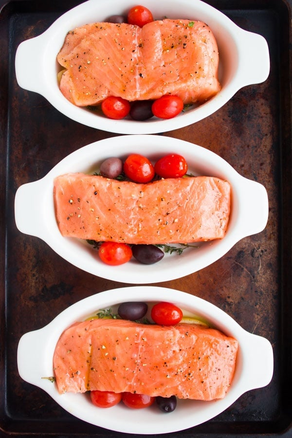 three individual casseroles with tomatoes and fresh salmon fillets ready to be baked