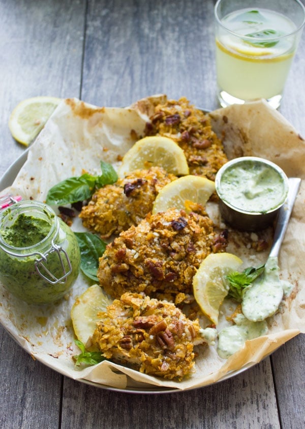 overhead shot of Pecan Crust Baked Chicken Tenders served on parchment paper with a small bowl with basil dip and pesto on the side