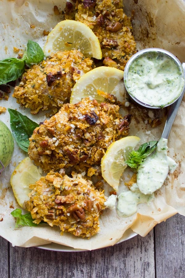 overhead shot of Pecan Crust Baked Chicken Tenders arranged with lemon slices and fresh basil served on parchment paper with a small bowl with basil dip on the side