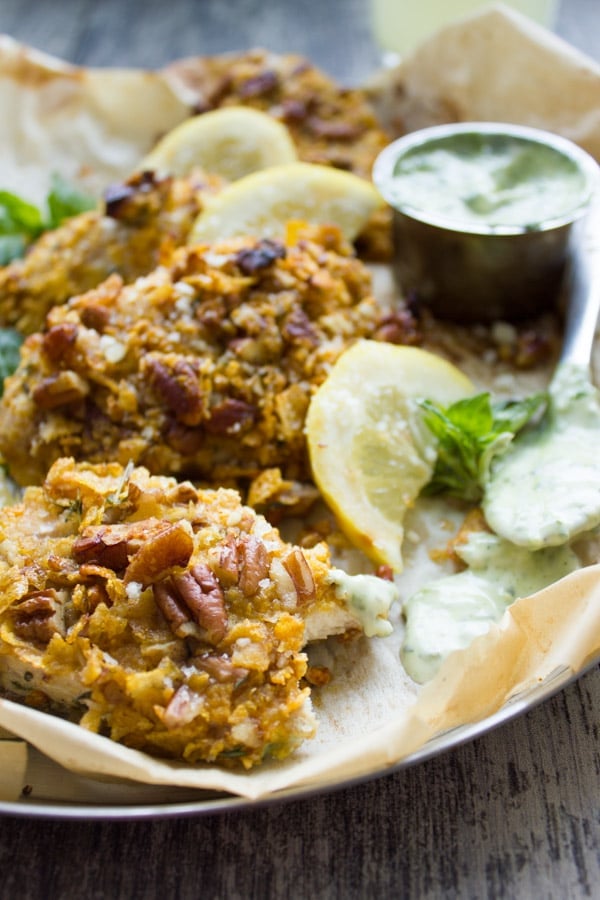 close-up of Pecan Crust Baked Chicken Tenders served on parchment paper with a small bowl with basil dip on the side